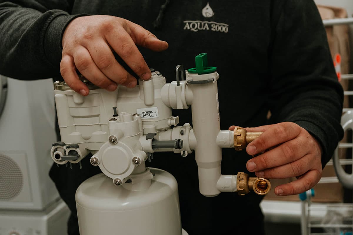 Technicien AQUA 2000 réglant la vanne d'un adoucisseur d'eau